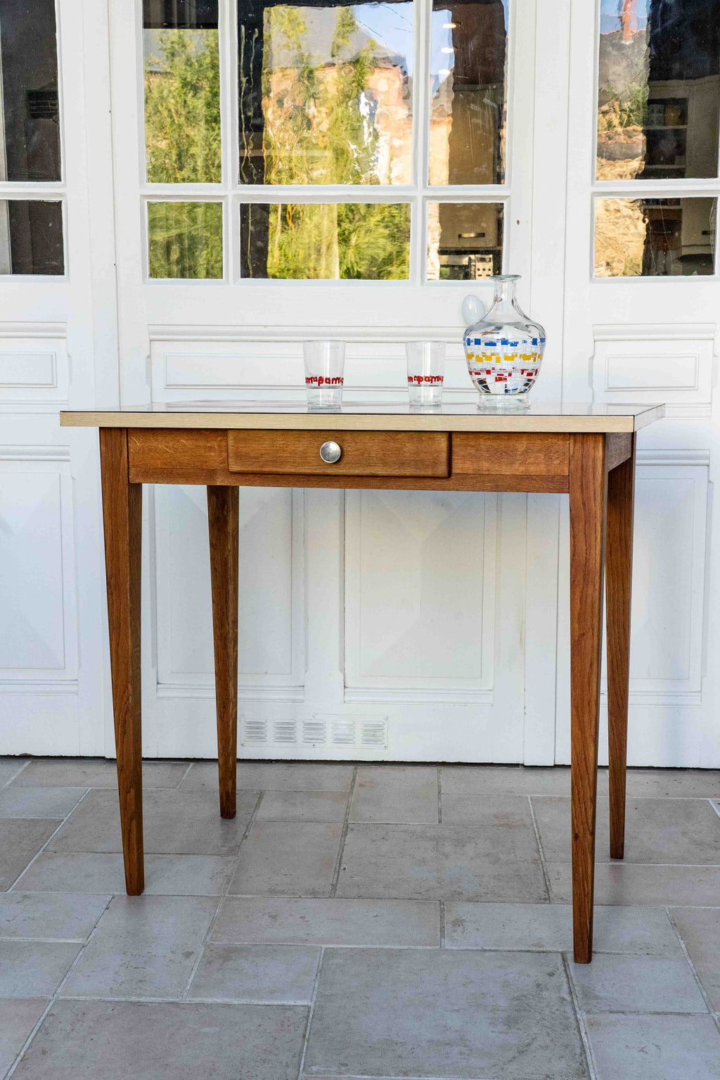 table en formica années 60 avec deux verres et une carafe dans une véranda