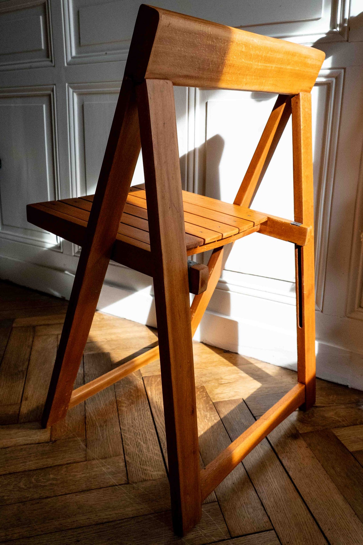 chaise en bois pliante, vue de dos, dans une entrée maison bourgeoise, soleil